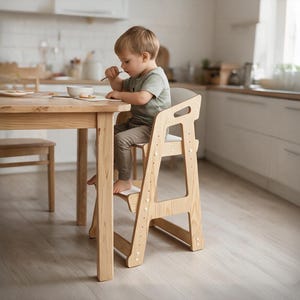 Könnte beinhalten: Ein heller Holz-Hochstuhl mit verstellbarem Sitz und Fußstütze, der sich durch ein stabiles A-Rahmen-Design mit weißen Akzenten auszeichnet. Der Stuhl steht an einem Holzesstisch und bietet eine stabile Sitzgelegenheit für ein Kleinkind.