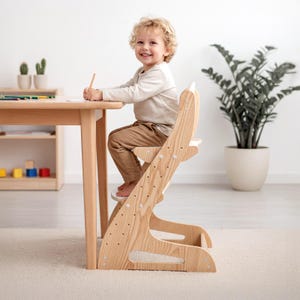 May include: A light-coloured wooden high chair with an adjustable seat and footrest, featuring a curved backrest and a sturdy frame. The chair is positioned at a matching wooden table, showcasing a natural wood grain finish and visible metal screws.