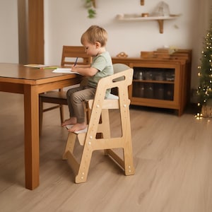 Puede incluir: Una torre de aprendizaje de madera clara con diseño de taburete, que cuenta con paneles laterales ajustables y una plataforma plana para estar de pie. La estructura está hecha de madera lisa con acabado natural y herrajes blancos.