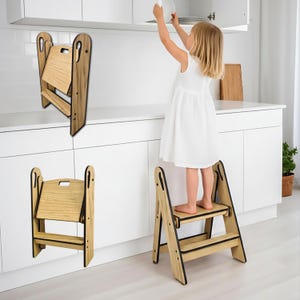 Peut inclure: Un escabeau pliant en bois à deux marches et une poignée. L'escabeau est en bois clair avec des accents noirs. Le tabouret est utilisé par un enfant qui atteint une étagère.