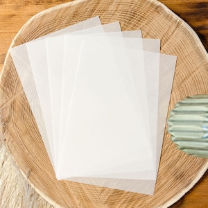 May include: Four sheets of white translucent paper on a wooden surface.