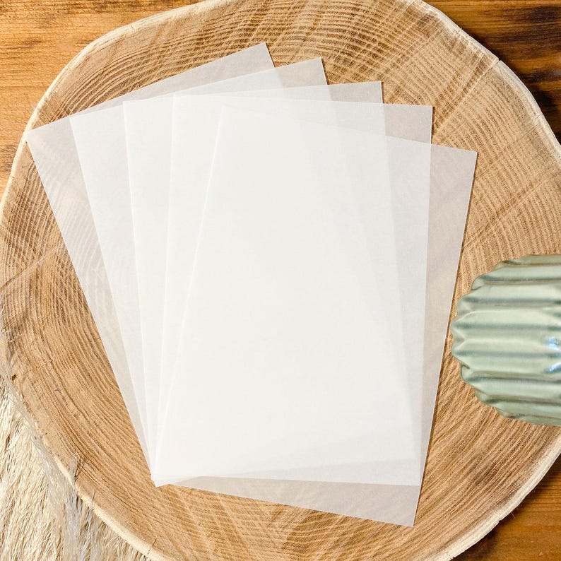 May include: Four sheets of white translucent paper on a wooden surface.