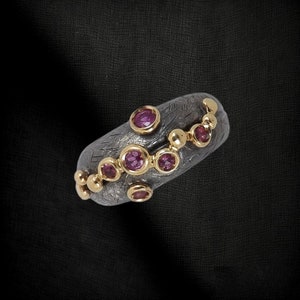 May include: A silver ring with a textured band and a row of small pink gemstones set in gold. The ring is decorated with a chain of gold beads.