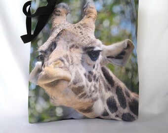 May include: A black canvas tote bag with a close-up image of a giraffe's face. The giraffe has a long neck, large brown eyes, and a spotted pattern.