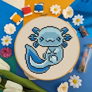 Peut inclure: Une broderie au point de croix bleue et blanche représentant un axolotl, un type de salamandre, avec une expression mignonne. L'axolotl est entouré de fleurs blanches et d'un fond bleu.