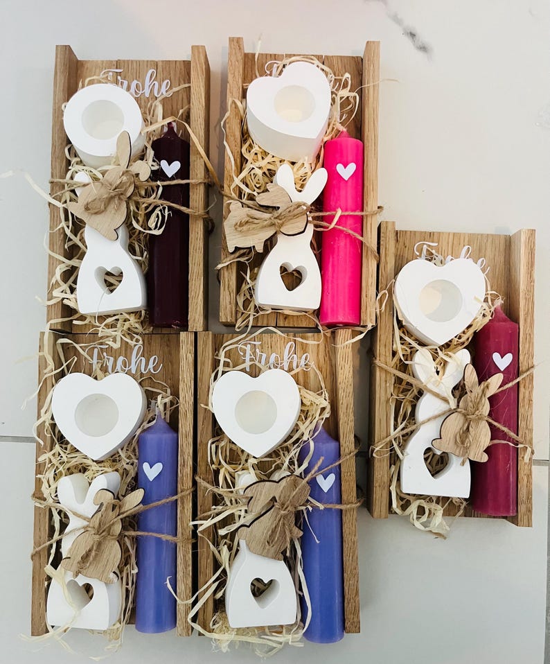 May include: Wooden candle holders with white heart-shaped candle holders, white bunny cutouts, and colored candles. The candles are purple, pink, and burgundy. The word "Frohe" is written on top of the wooden holders.