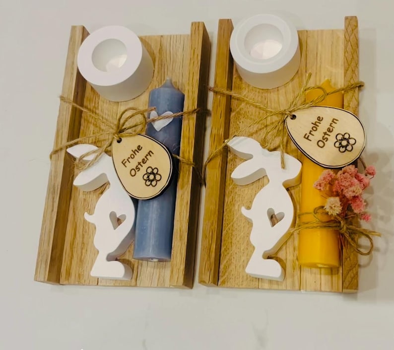 May include: Two wooden candle holders with candles, bunny cutouts, and tags that say "Frohe Ostern." One candle is blue, the other yellow. Each holder has a white tea light cup. The holders are tied with twine.