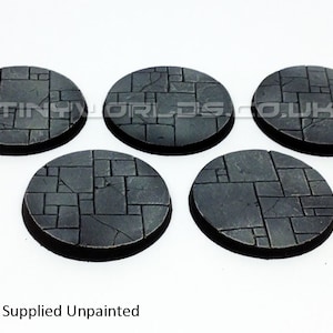 May include: Five unpainted, circular bases with a textured, stone-like pattern. The bases are dark grey with a black rim, and the surface is divided into irregular, rectangular shapes. The text "TINYWORLDS.CO.UK" is visible on the top.