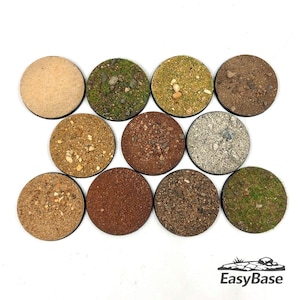 Puede incluir: Una colección de once bases circulares con diversas texturas, incluyendo arena, grava y parches de musgo verde. Las bases están diseñadas para figuras en miniatura y están dispuestas sobre un fondo blanco. El logotipo de EasyBase es visible.