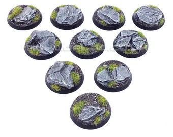 May include: A collection of ten miniature round bases, each featuring a gray rock formation surrounded by green grass. The bases have a dark brown border. The text "Product Supplied Unpainted" is at the bottom.