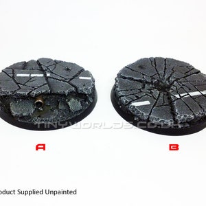 Peut inclure: Deux socles miniatures non peints avec un motif d'asphalte fissuré. Chaque socle est rond avec un bord noir et une surface texturée détaillée. L'un des socles comporte un tuyau et l'autre un marquage routier blanc. Le texte "Product Supplied Unpainted" est en bas.