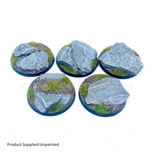 May include: Five circular miniature bases featuring textured grey rock formations and patches of green static grass. Each base has a black rim and a detailed, uneven surface designed for tabletop gaming figures. The text Product Supplied Unpainted is visible.
