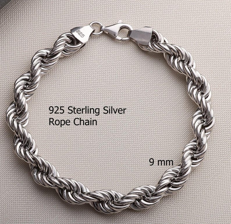 Pode incluir: Uma pulseira de corrente de corda em prata esterlina 925 de 9 mm com um fecho lagosta. O metal tem um acabamento polido e reflexivo. O texto 925 Sterling Silver Rope Chain e 9 mm est&aacute; impresso na imagem, indicando o material e a largura.