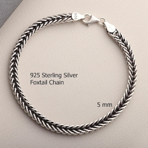 May include: A 925 sterling silver foxtail chain bracelet with a lobster claw clasp. The metal links feature a woven, braided pattern with oxidized detailing. The text 925 Sterling Silver Foxtail Chain and 5 mm are visible on the image.
