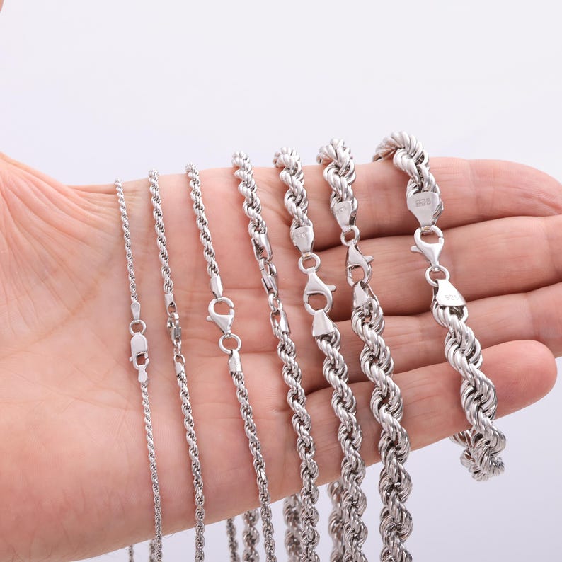 Pode incluir: Uma cole&ccedil;&atilde;o de sete correntes de corda em tom prateado de espessuras variadas, cada uma com um fecho lagosta e uma pequena etiqueta de metal estampada com 925, dispostas em fila da mais fina para a mais grossa para mostrar a gama de tamanhos.