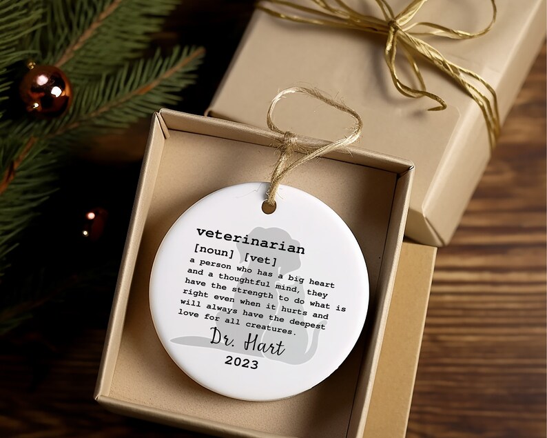 May include: White ceramic ornament with a silhouette of a dog and the text "veterinarian [noun] [vet] a person who has a big heart and a thoughtful mind, they have the strength to do what is right even when it hurts and will always have the deepest love for all creatures. Dr. Hart 2023"