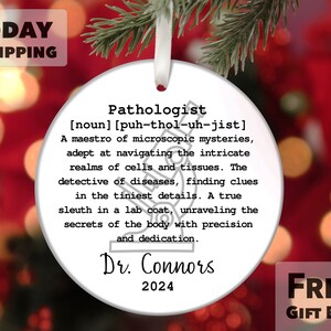 May include: White round Christmas ornament with a black and white illustration of a microscope and the text "Pathologist [noun] [puh-thol-uh-jist] A maestro of microscopic mysteries, adept at navigating the intricate realms of cells and tissues. The detective of diseases, finding clues in the tiniest details. A true sleuth in a lab coat, unraveling the secrets of the body with precision and dedication. Dr. Connors 2024"