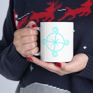 May include: White ceramic mug with a turquoise blue spiral design. The mug is being held by a person wearing a blue and red sweater.