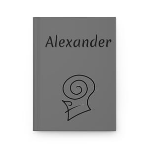 May include: A gray journal with the name "Alexander" printed in black script at the top. Below the name is a black line drawing of a stylized head with a spiral design.