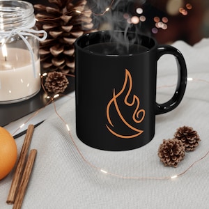 May include: Black ceramic mug with a stylized orange flame design. The mug is filled with coffee and steam is rising from the top.