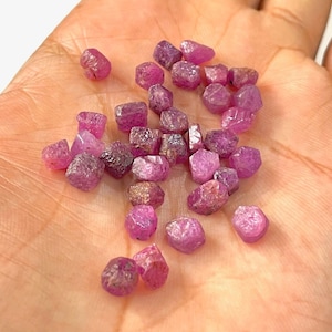 Peut inclure: Une collection de petits cristaux de rubis roses de formes et de tailles variées. Les cristaux sont bruts et ont un aspect naturel non poli.