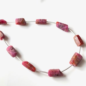 Puede incluir: Una hebra de cuentas de rubí rosa enhebradas en un alambre de plata. Las cuentas son facetadas y tienen una textura rugosa y natural.