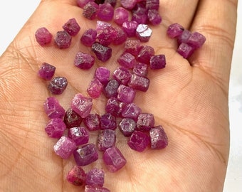 Può includere: Una collezione di piccole pietre preziose di rubino sfaccettate in varie tonalità di rosa e rosso. Le pietre preziose sono esposte su una mano, mostrando le loro dimensioni e forma.