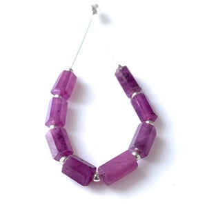 May include: A strand of faceted, deep magenta-colored gemstone beads. Each bead is a rectangular shape with cut edges, connected by a thin silver wire. The beads are strung together with small silver spacer beads, creating a necklace or bracelet.