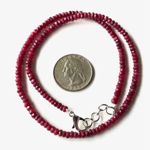 May include: A delicate necklace composed of small, faceted, deep red gemstones. The necklace is secured with a silver-colored clasp. A U.S. quarter coin is included for size reference. The coin is dated 1998.