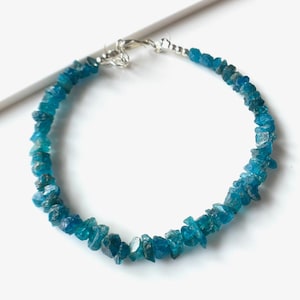 Pode incluir: Um bracelete de apatita azul com fecho de prata. O bracelete é feito de pequenas pedras de forma irregular.