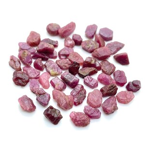Puede incluir: Una colección de piedras preciosas de rubí en bruto de color rosa y rojo. Las piedras preciosas en bruto son de varias formas y tamaños.