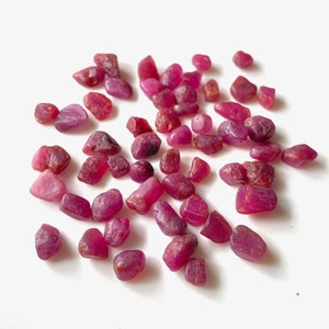 Puede incluir: Una colección de piedras preciosas de rubí rosa sueltas. Los rubíes son de varios tamaños y formas, algunos tienen una forma más redondeada y otros son más angulares.