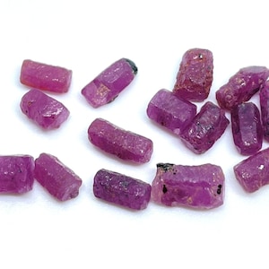 May include: A collection of 14 rough, unpolished ruby gemstones. The rubies are a deep pink color and have a natural, irregular shape. They are perfect for jewelry making or crystal healing.