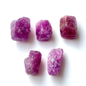 Pode incluir: Cinco pedras preciosas de rubi rosa brutas. As pedras preciosas são de vários tamanhos e formas, algumas têm uma forma mais quadrada e outras mais arredondadas.