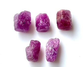 Può includere: Cinque pietre preziose di rubino rosa grezze. Le pietre preziose sono di varie dimensioni e forme, alcune hanno una forma più quadrata e altre più arrotondate.
