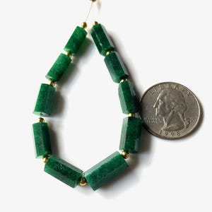 May include: A strand of faceted, emerald green gemstone beads with gold-colored spacers. The beads are arranged in a teardrop shape. A U.S. quarter coin is next to the beads for size comparison. The beads are on a white background.