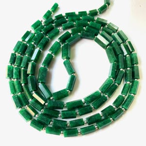 Op de afbeelding: Een ketting bestaande uit gefacetteerde, smaragdgroene edelsteen kralen. De kralen zijn rechthoekig met meerdere zijden en zijn geregen met kleine, zilverkleurige kralen. De ketting wordt getoond tegen een witte achtergrond.