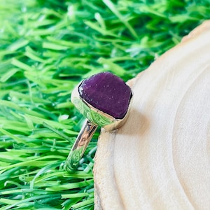 May include: A silver ring with a large, faceted, purple gemstone set in a bezel setting.