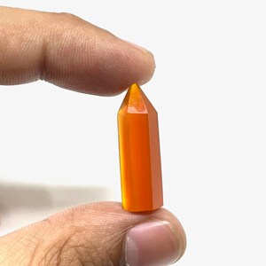 Può includere: Una punta di cristallo sfaccettata di colore arancione brillante. La punta è lunga circa 5 cm ed è tenuta tra due dita.