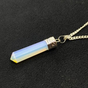 May include: A silver chain necklace with a clear iridescent opal crystal pendant. The pendant is shaped like a long, thin point.