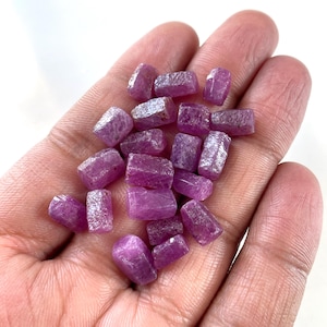 Puede incluir: Un puñado de piedras preciosas de rubí rosa en bruto. Las piedras sin pulir muestran una superficie natural y texturizada, con formas variadas. Estas piedras preciosas son ideales para la fabricación de joyas o coleccionar.