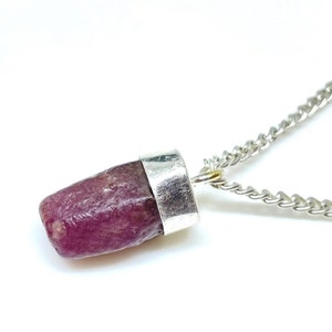 Può includere: Una collana con catena d'argento con un ciondolo che presenta una pietra preziosa di rubino rosa grezza incastonata in una montatura d'argento.