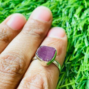 May include: A silver ring with a purple gemstone. The ring is set on a green grassy background.
