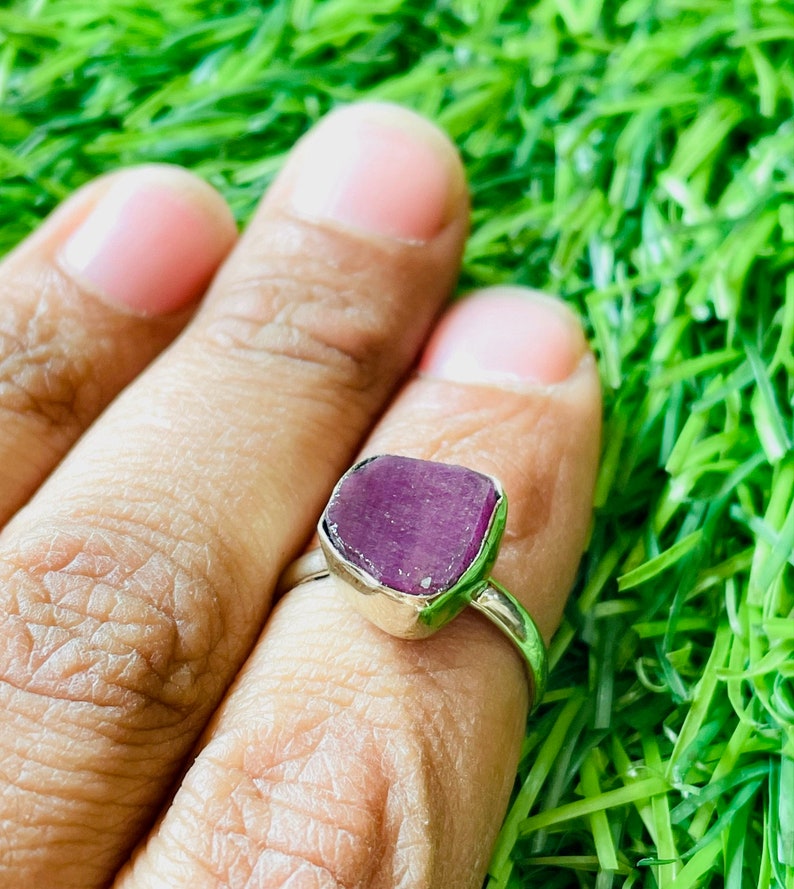 May include: A silver ring with a purple gemstone. The ring is set on a green grassy background.