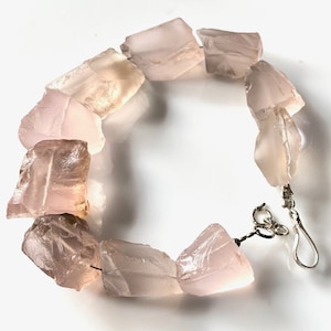 May include: A bracelet made of light pink, faceted, natural quartz crystals. The bracelet is strung on a silver chain with a lobster clasp.