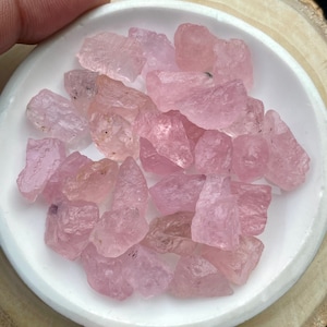 Puede incluir: Una colecci&oacute;n de piedras preciosas rosadas, sin cortar y en bruto, en un plato de cer&aacute;mica blanca. Las piedras preciosas son de varios tama&ntilde;os y formas.
