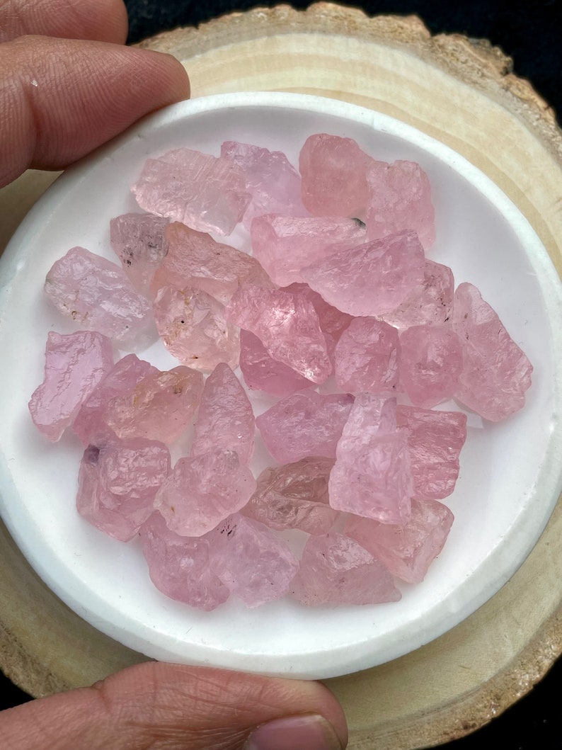 Puede incluir: Una colecci&oacute;n de piedras preciosas rosadas, sin cortar y en bruto, en un plato de cer&aacute;mica blanca. Las piedras preciosas son de varios tama&ntilde;os y formas.