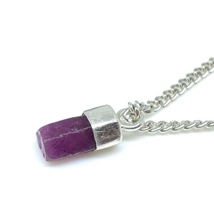 Op de afbeelding: Een zilveren ketting met een hanger met een ruwe paarse edelsteen.