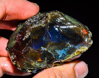 May include: A large, rough, iridescent opal with a dark brown, blue, and green color pattern. The opal is translucent and has a glossy finish.