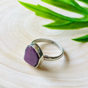 May include: A silver ring with a purple gemstone set in a triangular shape.